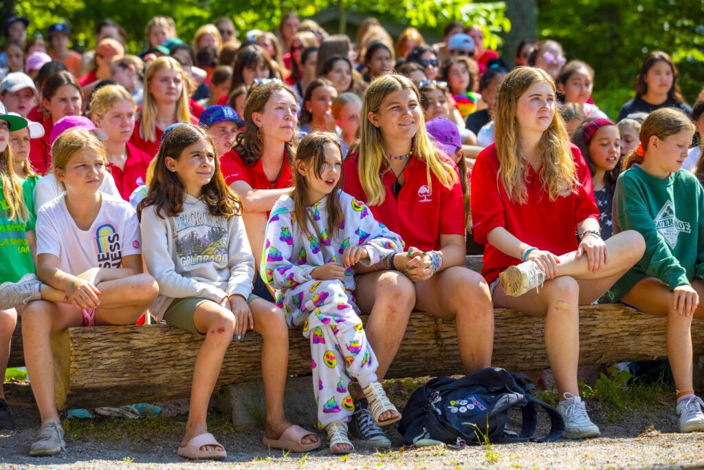 Campers and staff sitting together on a large wooden log.