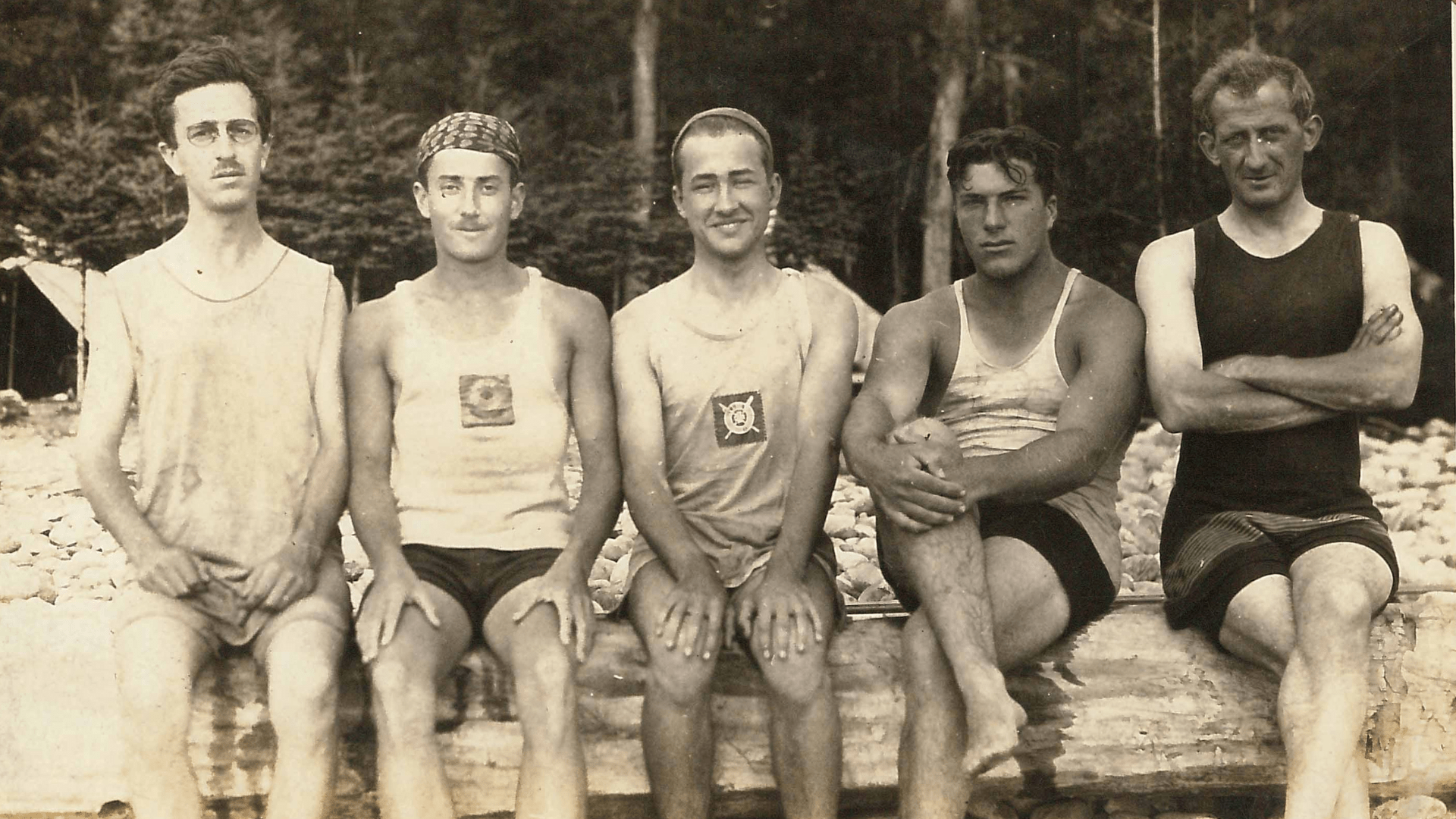 Three young men in athletic wear sitting on a log.