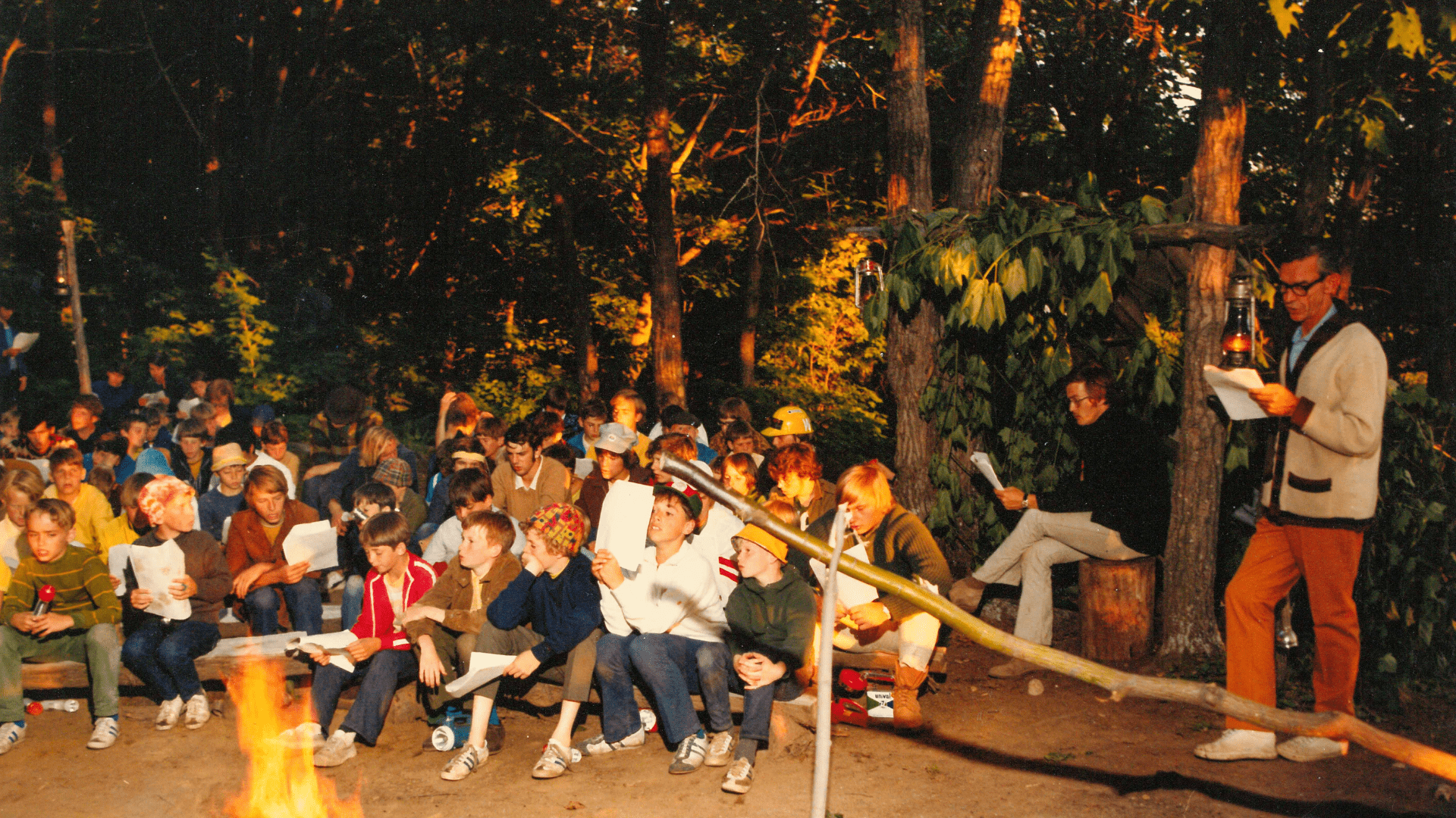 Vintage color photo of campers gathered around an evening campfire.