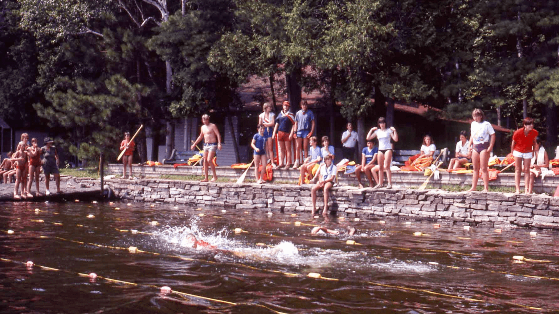 Campers swimming and jumping into a lake from wooden docks.