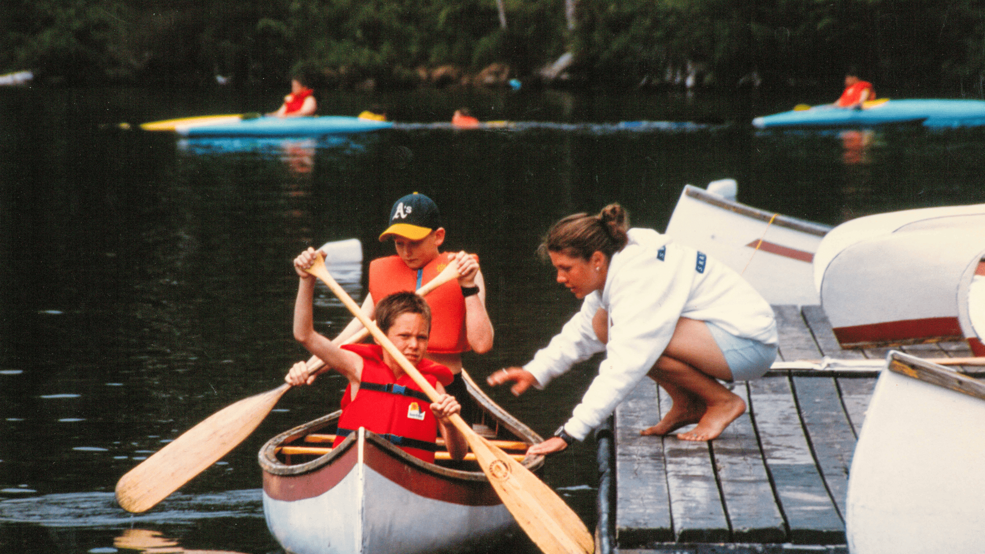 Two people helping a child into a red canoe.