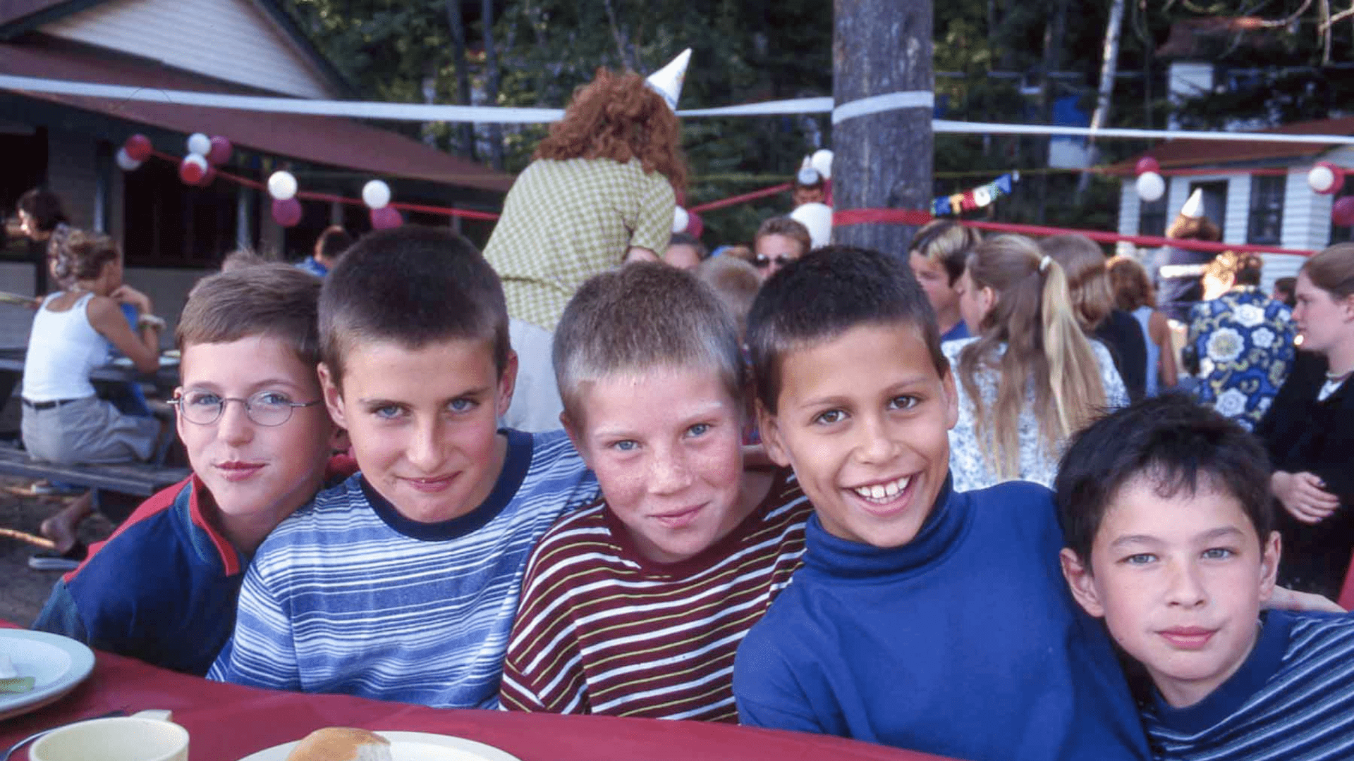 Three young boys smiling while sitting together in the outdoors.