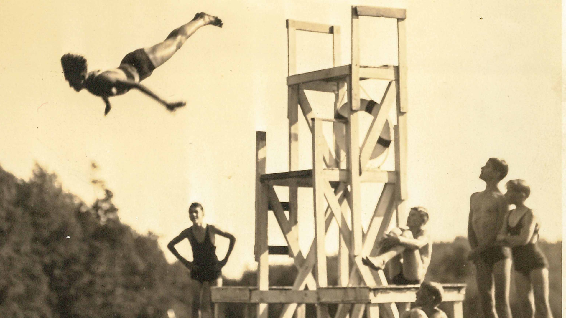 Sepia photo of someone diving from a high wooden tower.