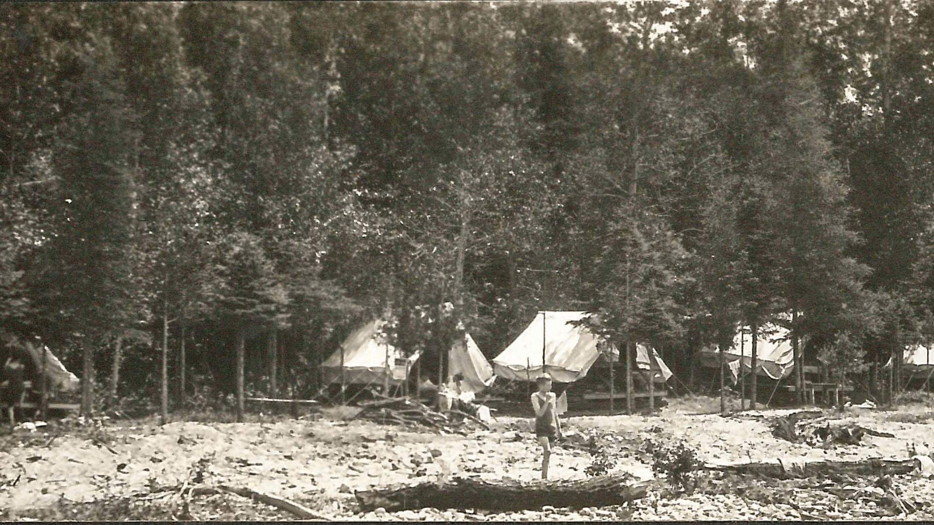 Sepia photo of canvas tents set up in a forest.