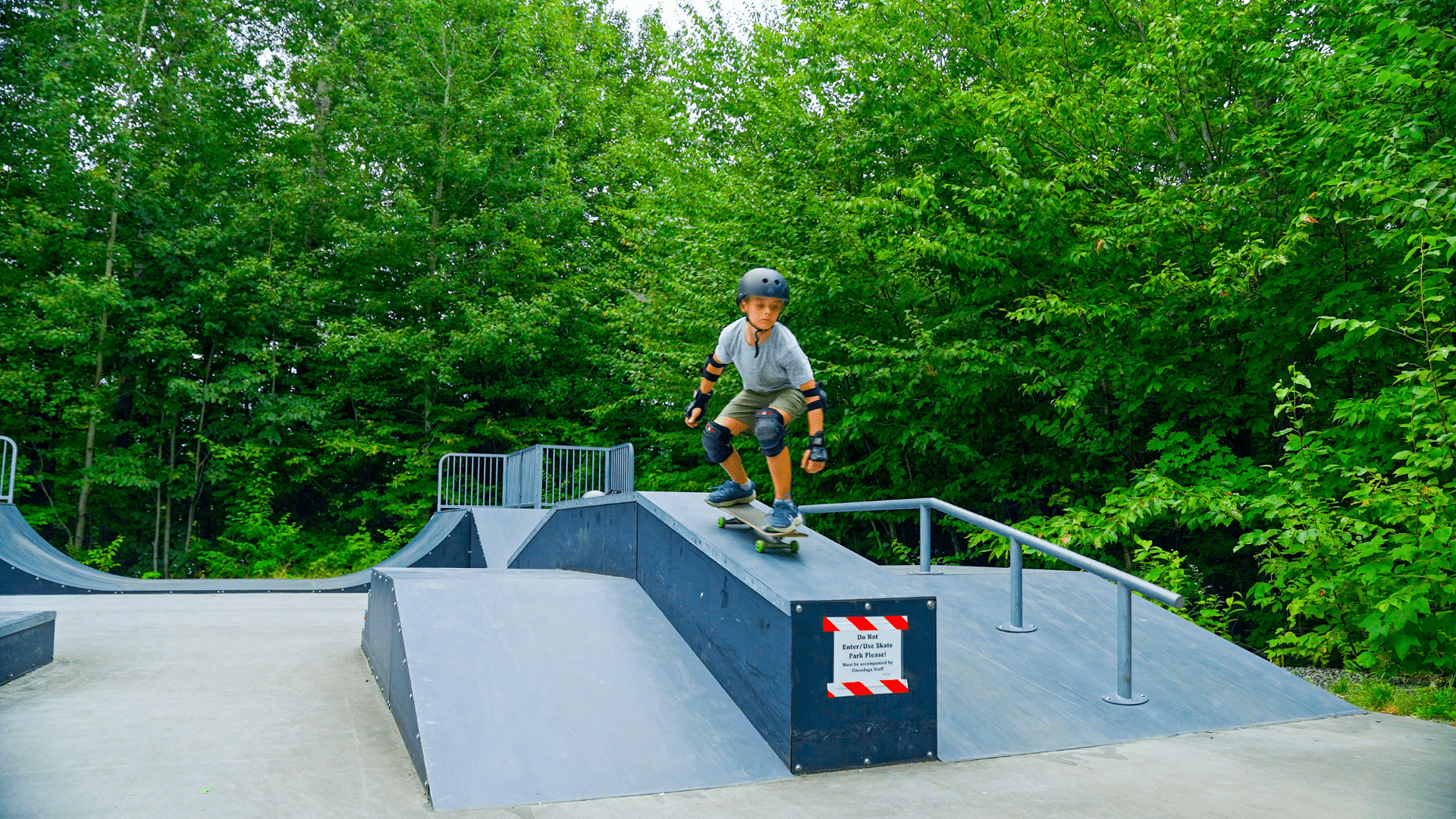 A young boy wearing safety gear skateboarding on a ramp.