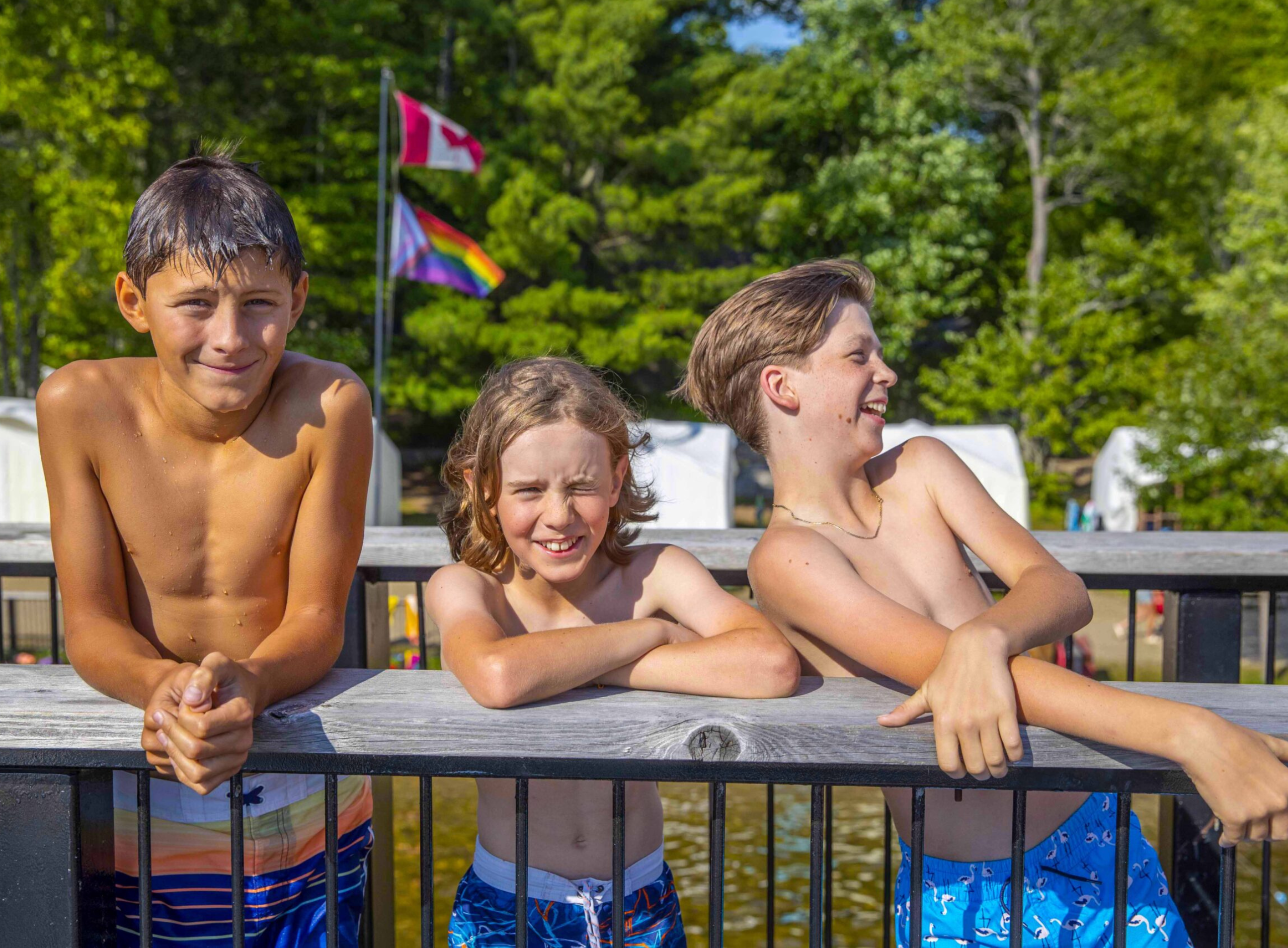 Three young boys smiling while leaning on a wooden fence.