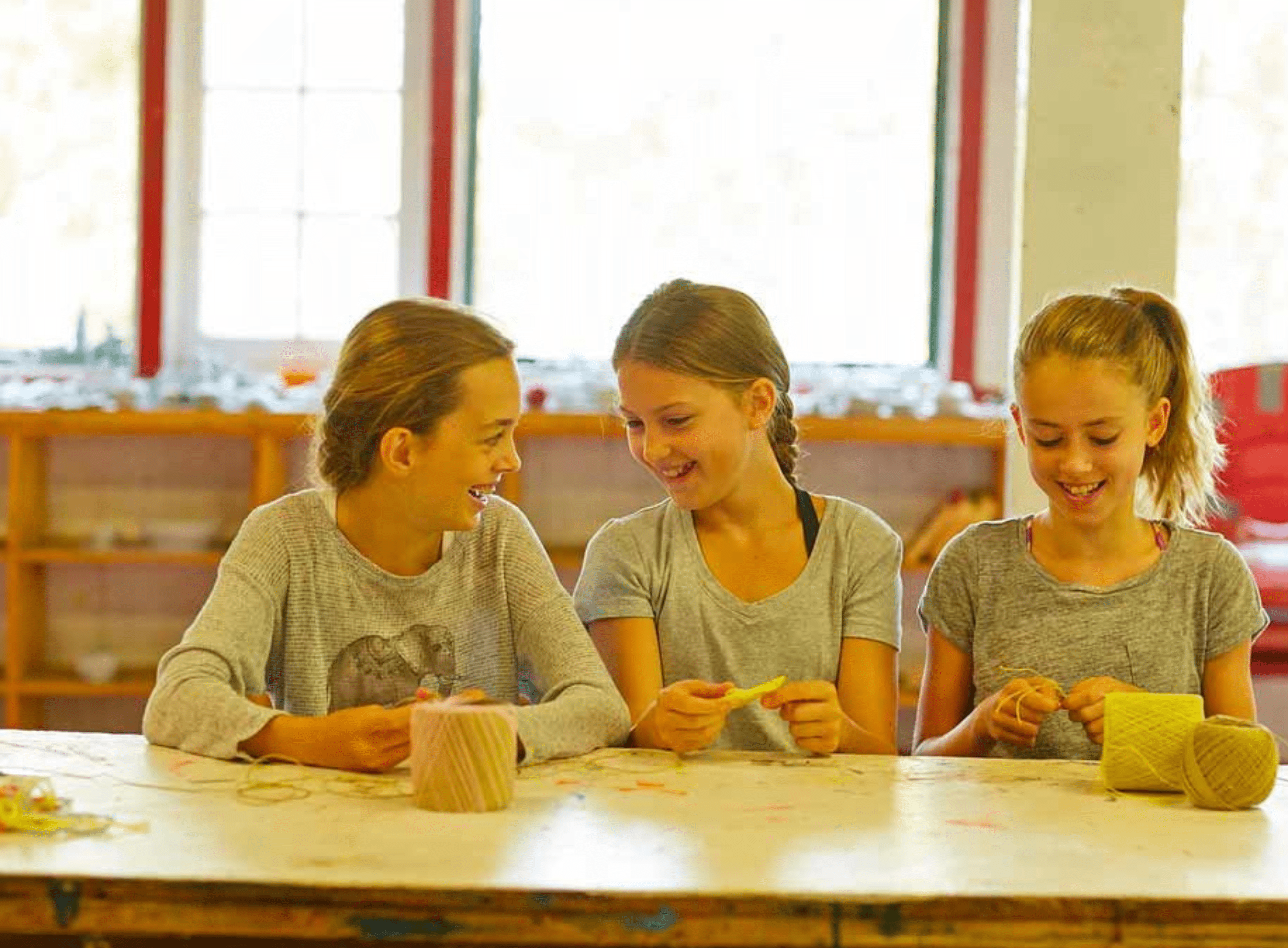 Three young girls smiling while working on an indoor craft.