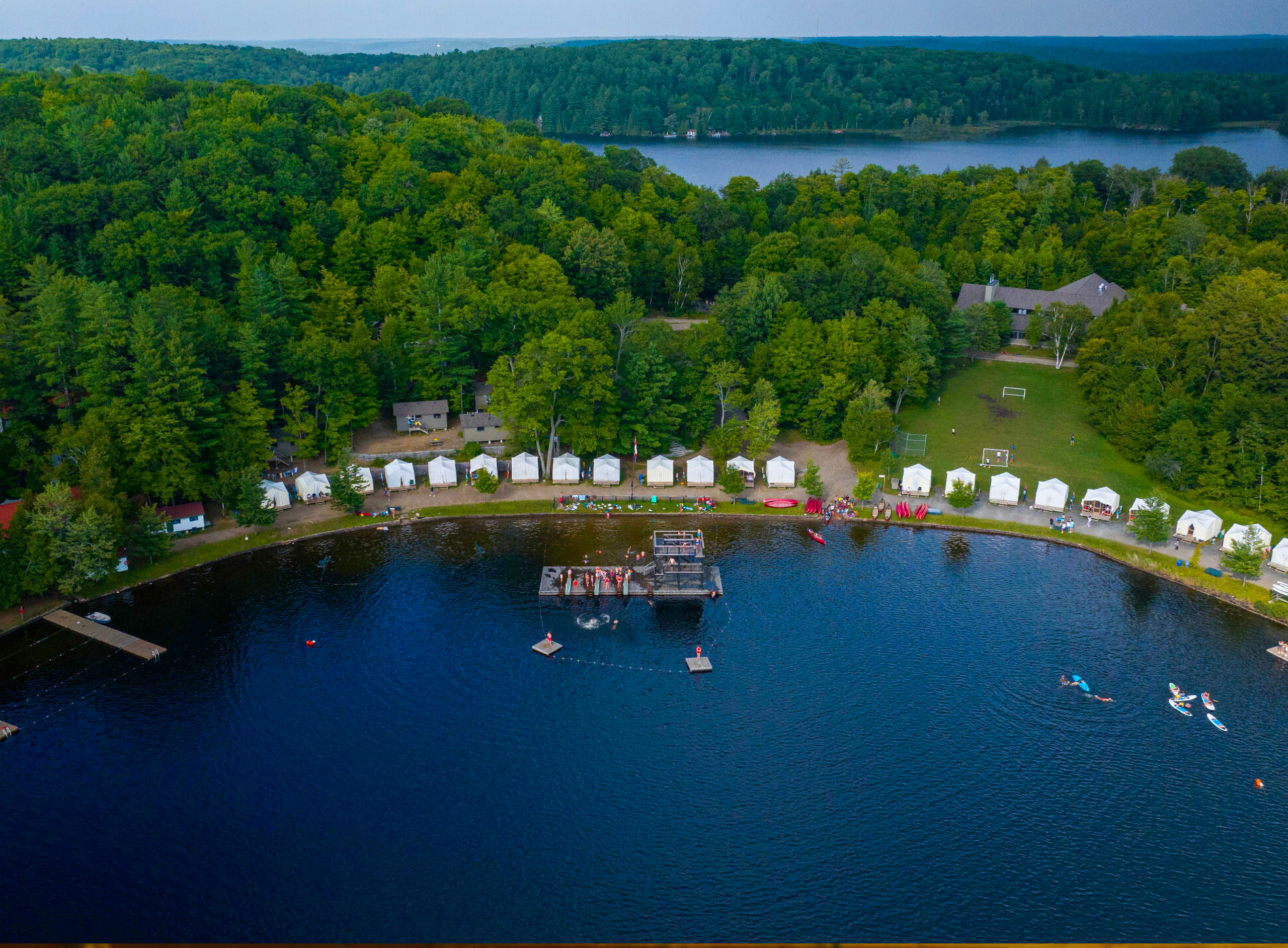 Aerial view of summer camp cabins along a blue lake.