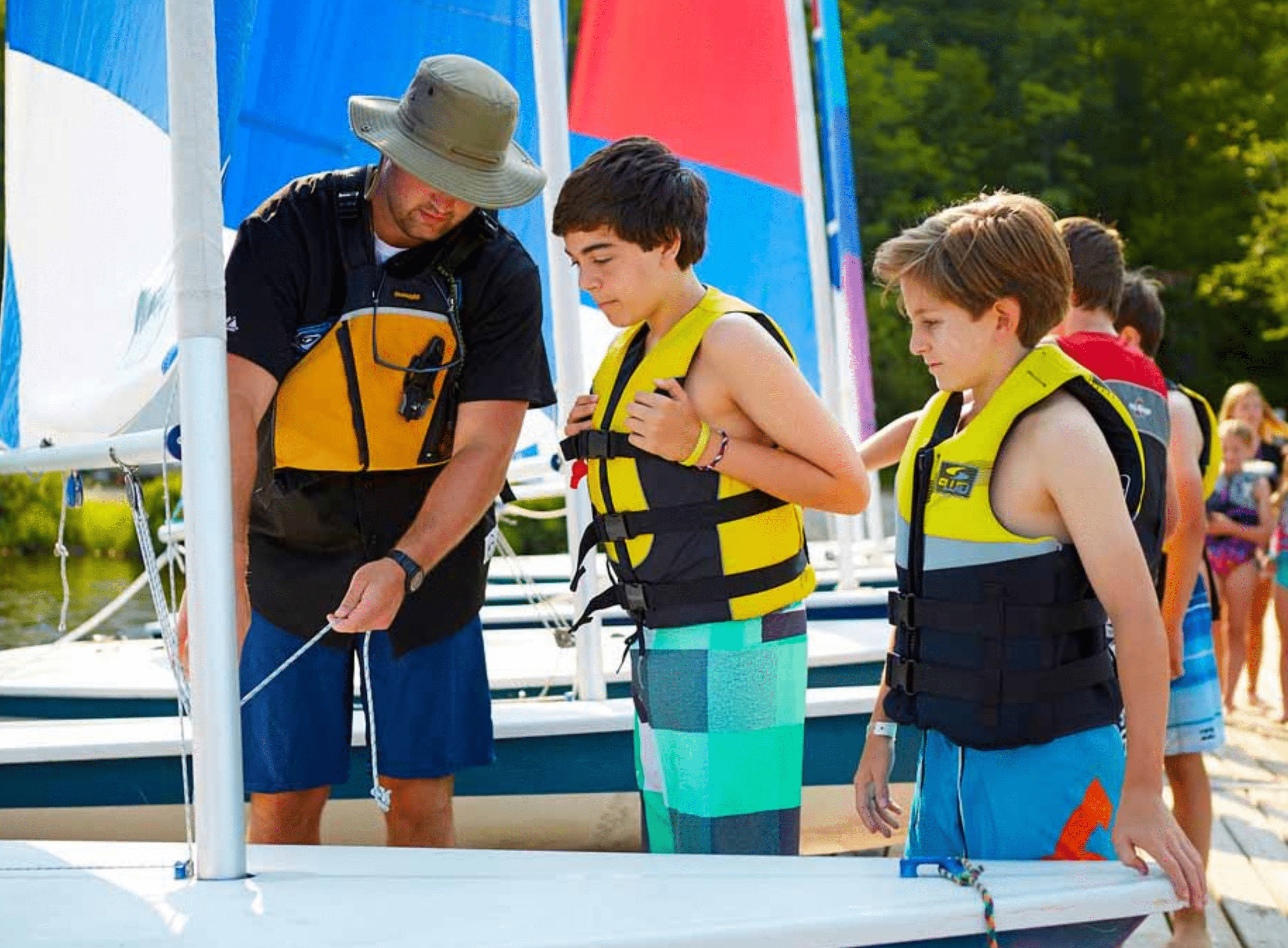 Instructor teaching two young boys how to operate a sailboat.