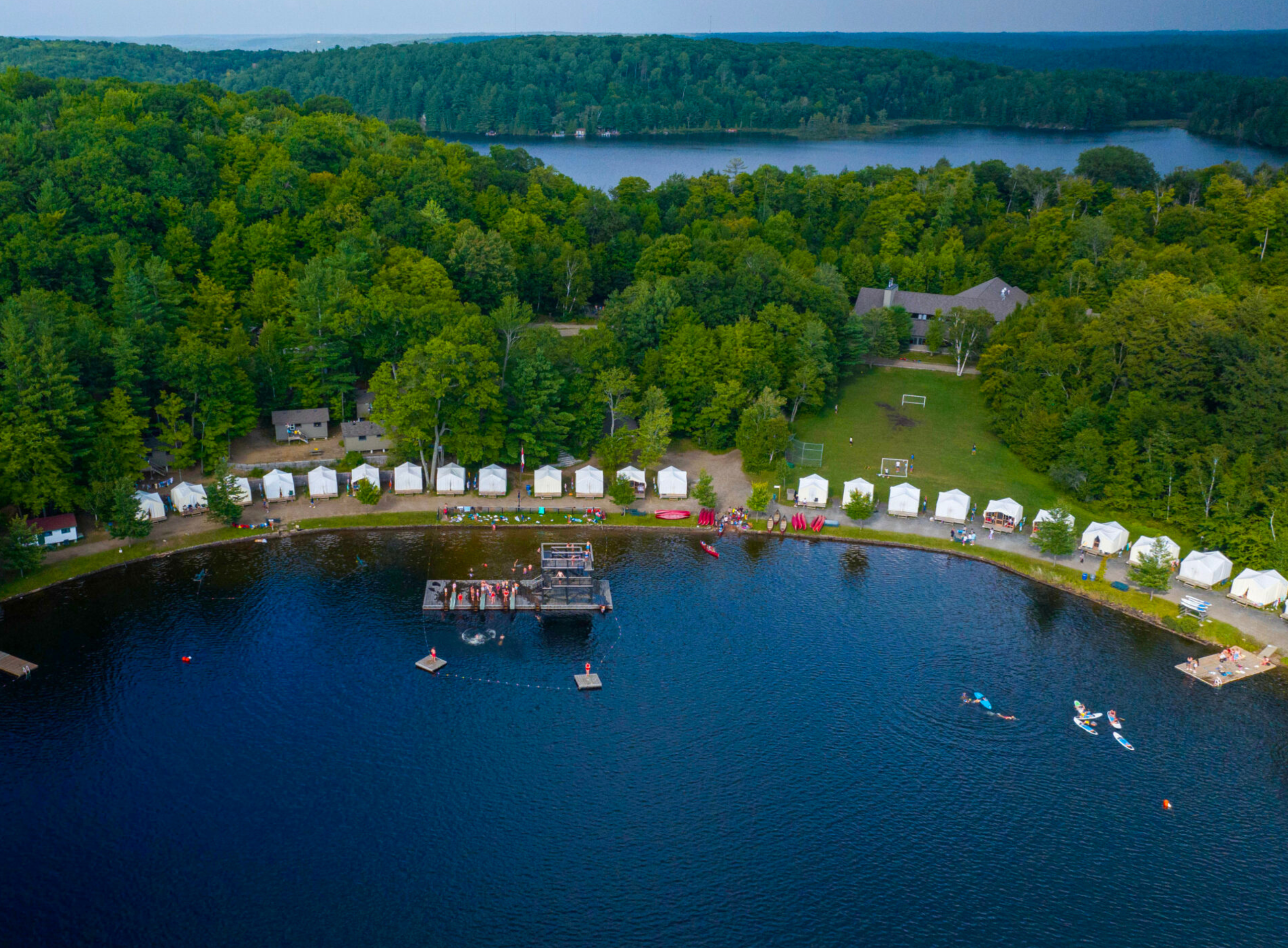Aerial view of a summer camp lakefront with white tents.