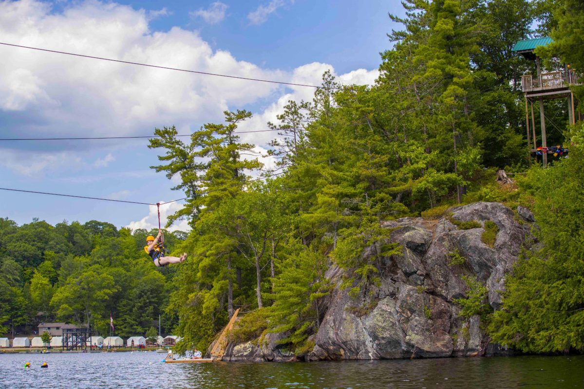 A person ziplining over water near a rocky tree shoreline.
