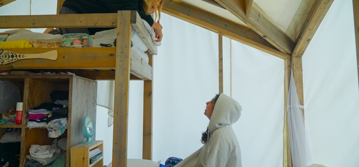 Campers talking between bunks inside a tent.