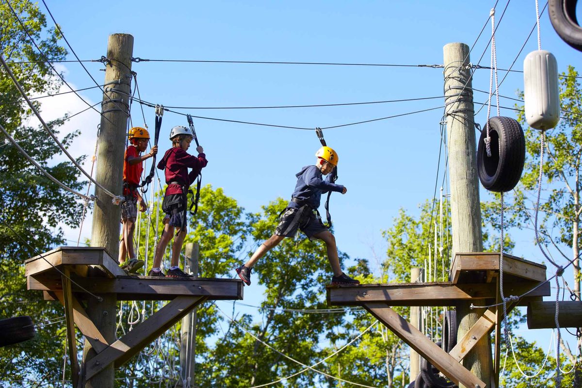 Two children carefully walking across an elevated outdoor ropes course.
